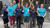 A group of Fight for Sight employees standing outside in tshirts in the brand colours - dark navy and teal - they are holding arms aloft and looking cheerful.