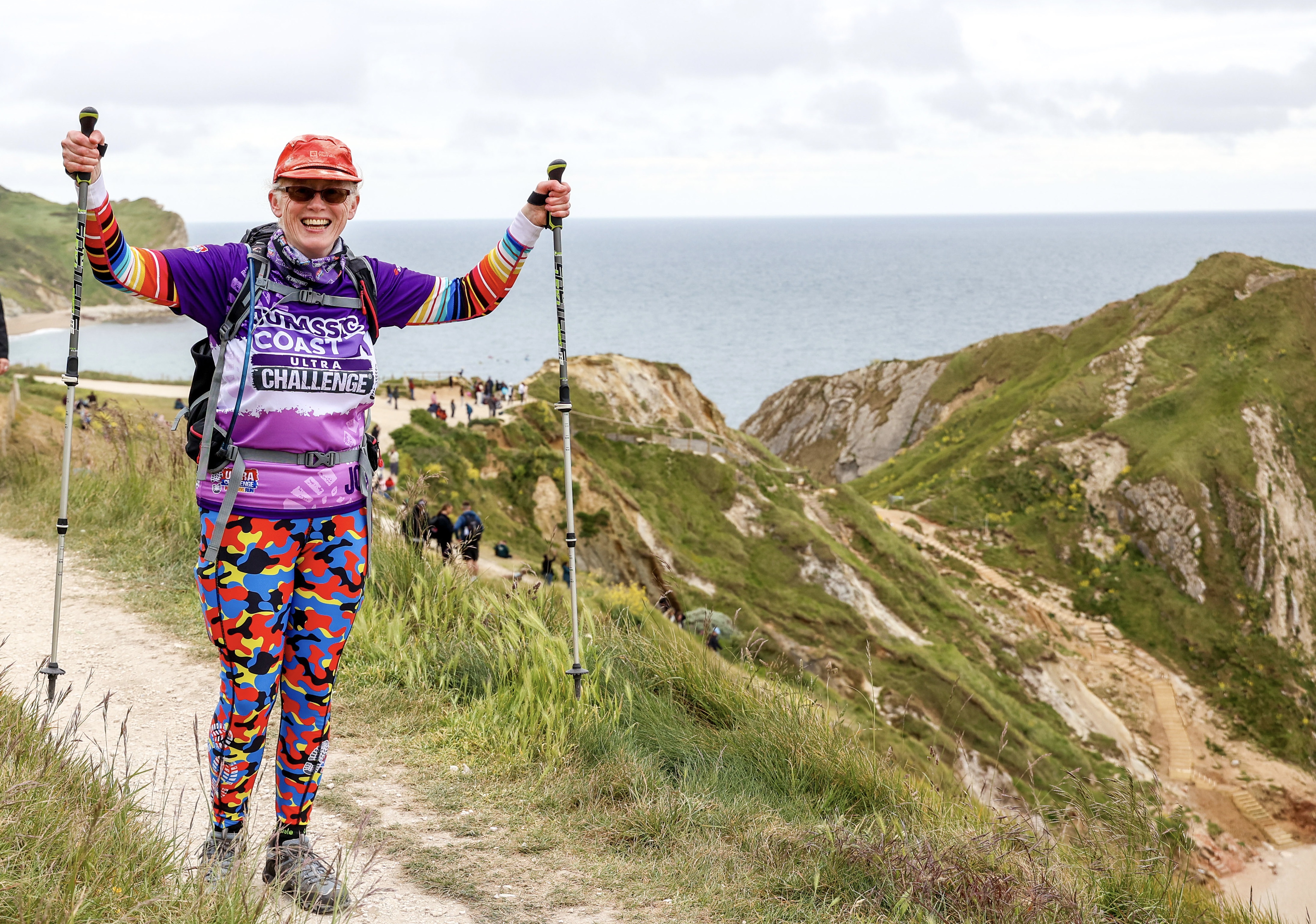 A walker smiling and waving with their walking poles while taking part in the Jurassic Coast Ultra Challenge