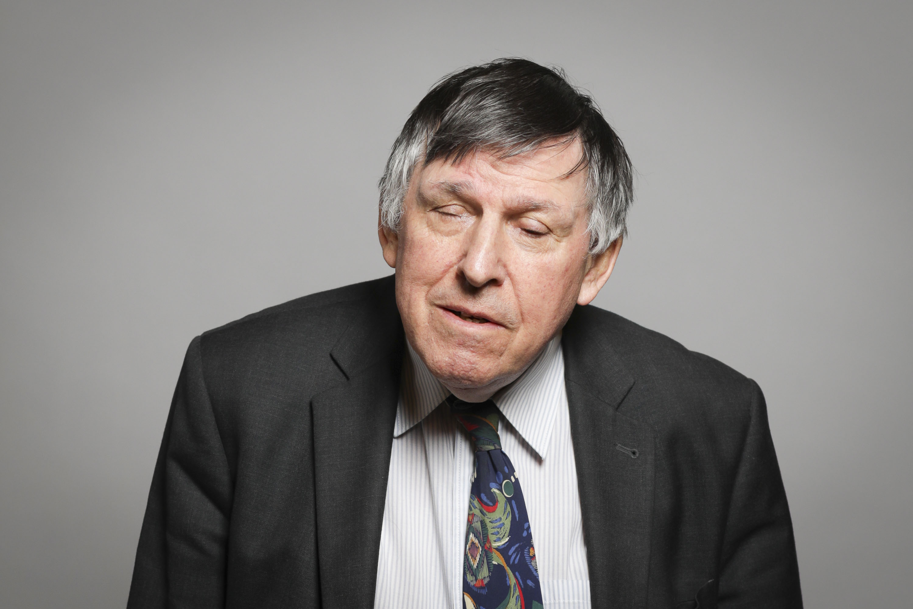 Lord Low of Dalston in a suit and tie standing in front of a grey background