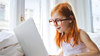 A young girl with ginger hair and glasses is working intently on a laptop
