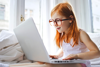 A young girl with ginger hair and glasses is working intently on a laptop