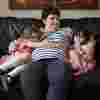 Charmaine, a white woman with short brown hair is snuggled up with her two daughters on a sofa. The girls are looking at the camera shyly, Charmaine is smiling proudly at her daughter who is sitting to her right.