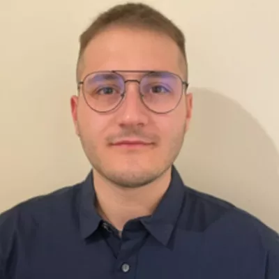 A headshot of Anastasios, a white man with short brown hair and glasses. He's lightly smiling at the camera. 