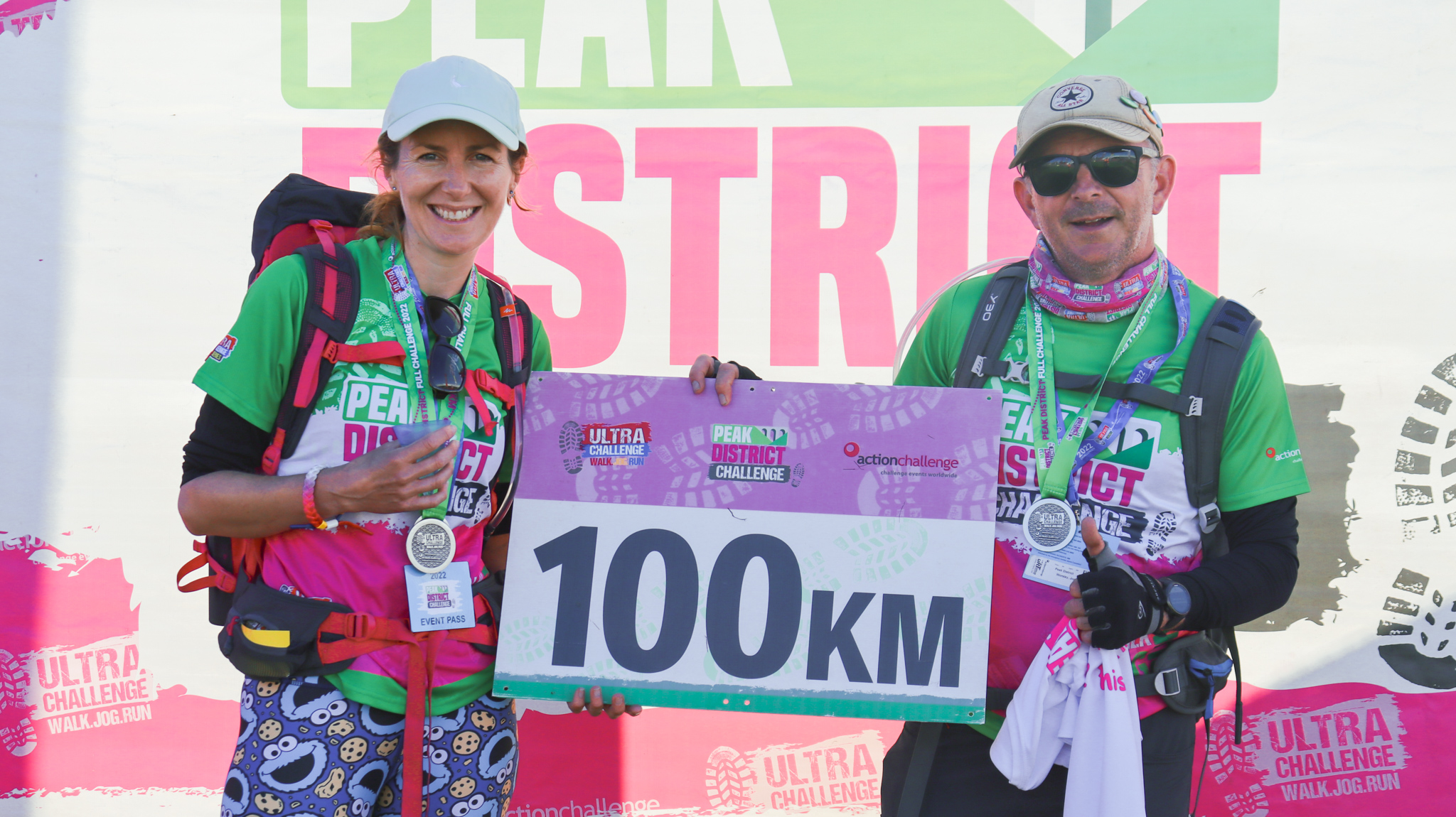 Finishers of the Peak District Ultra Challenge displaying their medals and t-shirts while holding a sign saying 100km