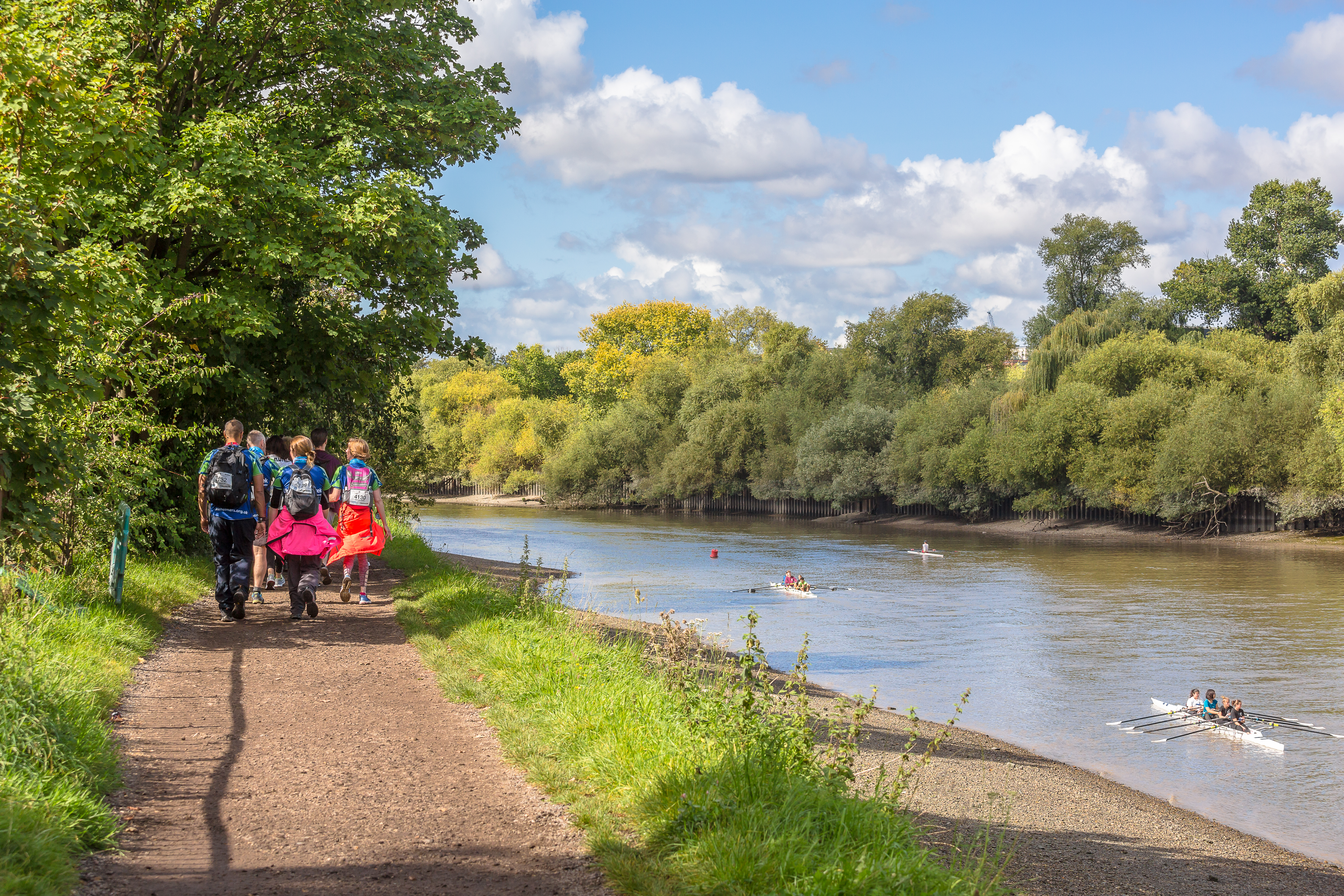 Walkers taking part in the Thames Path Ultra Challenge along the River Thames, with people rowing past