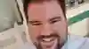 George is smiling open mouthed at the camera. He's wearing a tie and white lab coat.