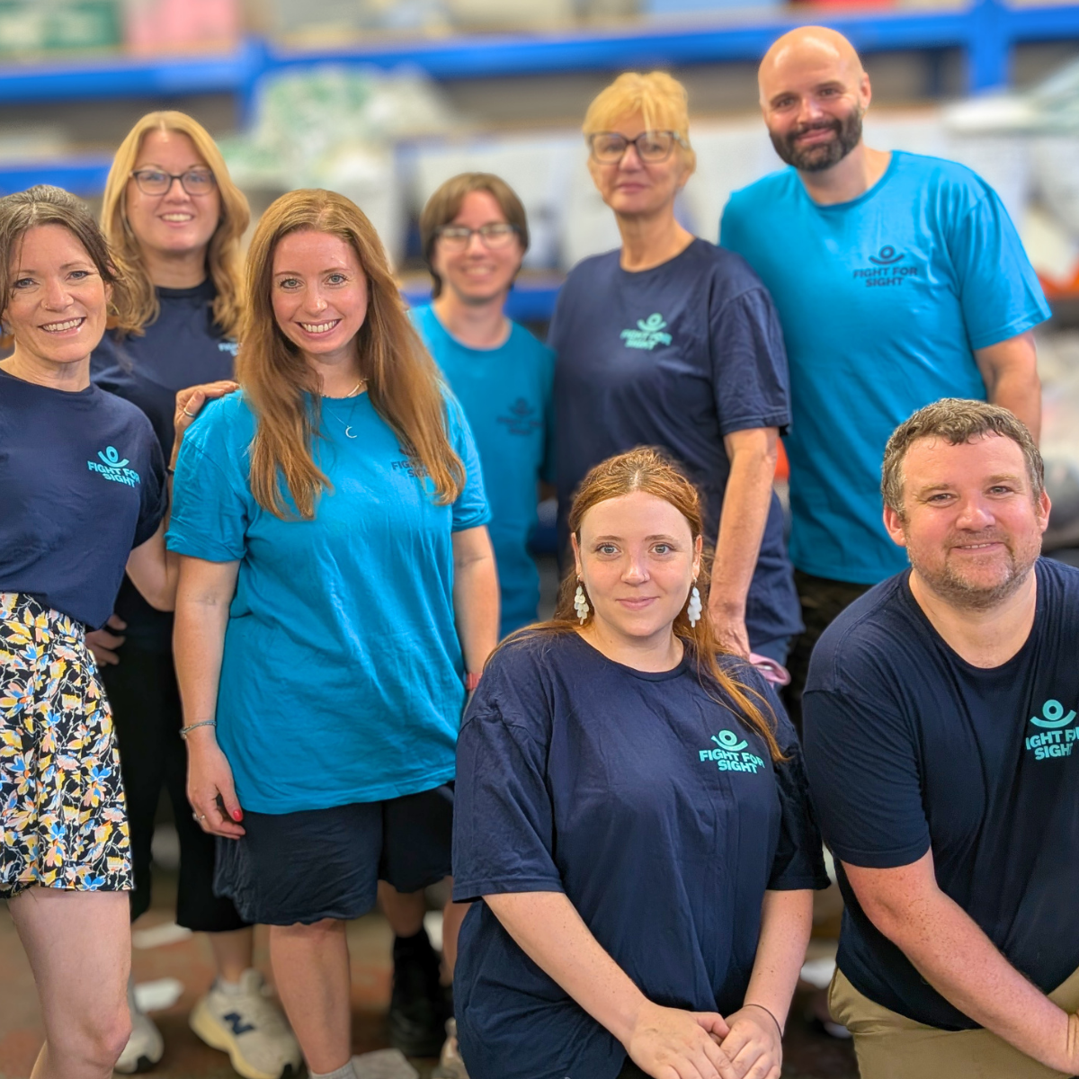 A group of Fight for Sight team members men and women wearing turquoise and navy branded tshirts, they are all smiling and grouped together.