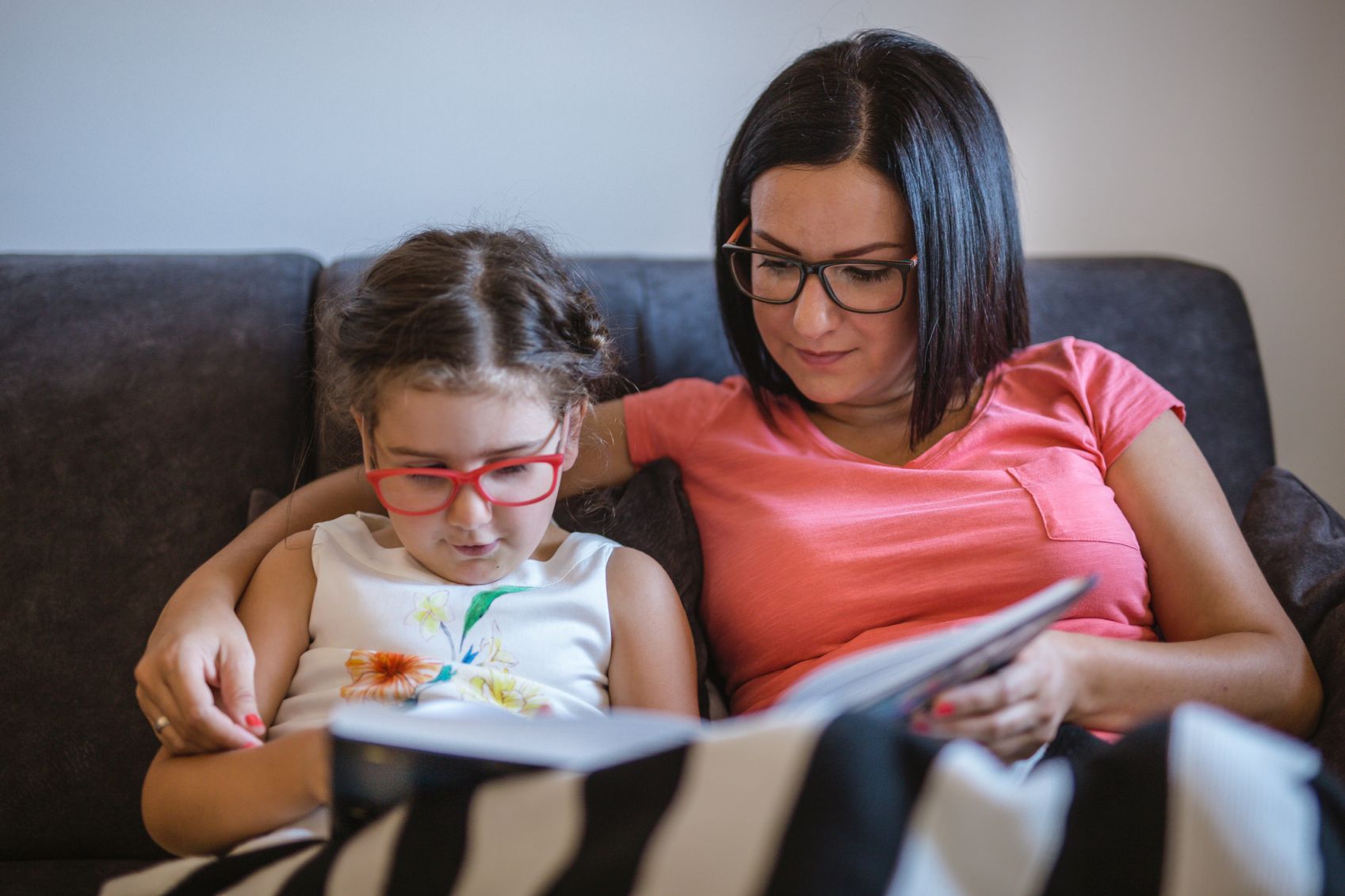 Mother and young child both wearing glasses reading a book together. 