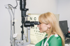 Funded researcher Jasmina Kapetanovic. Jasmina is looking through an ophthalmic device. Behind her is an eye chart.