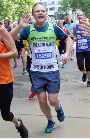 John running a half marathon for Fight for Sight. He's waving at the camera and wearing a green Fight for Sight branded vest, his running name is The Codd Father