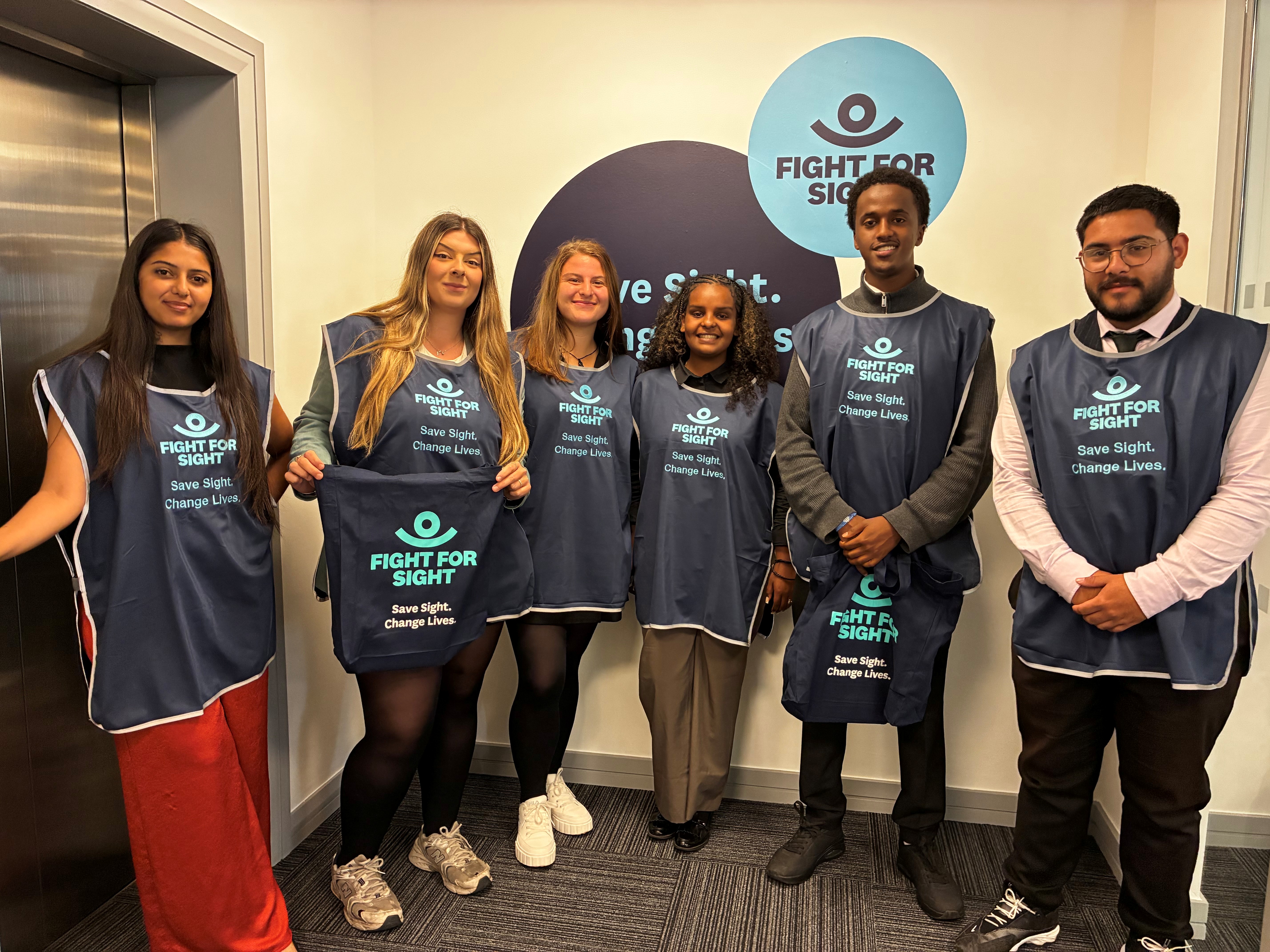 An image of six Fight for Sight fundraisers, wearing the Fight for Sight tabards, looking to camera and smiling.
