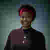 Shakirat has a warm smile and a purple headband and is pictured against a muted gray backdrop.  