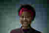 Shakirat has a warm smile and a purple headband and is pictured against a muted gray backdrop.  