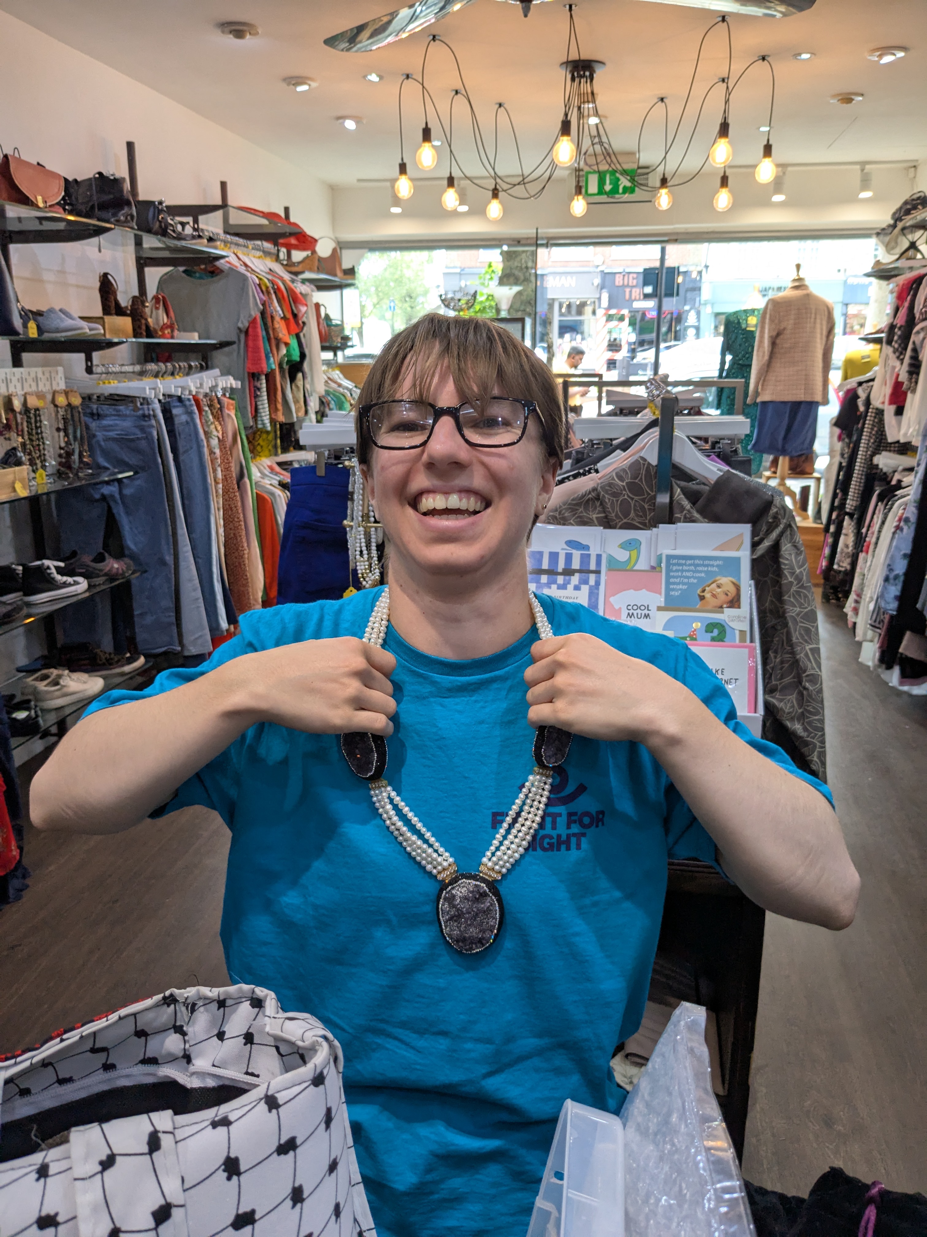 Louis in Chiswick charity shop in Fight for Sight tshirt laughing wearing a donation necklace