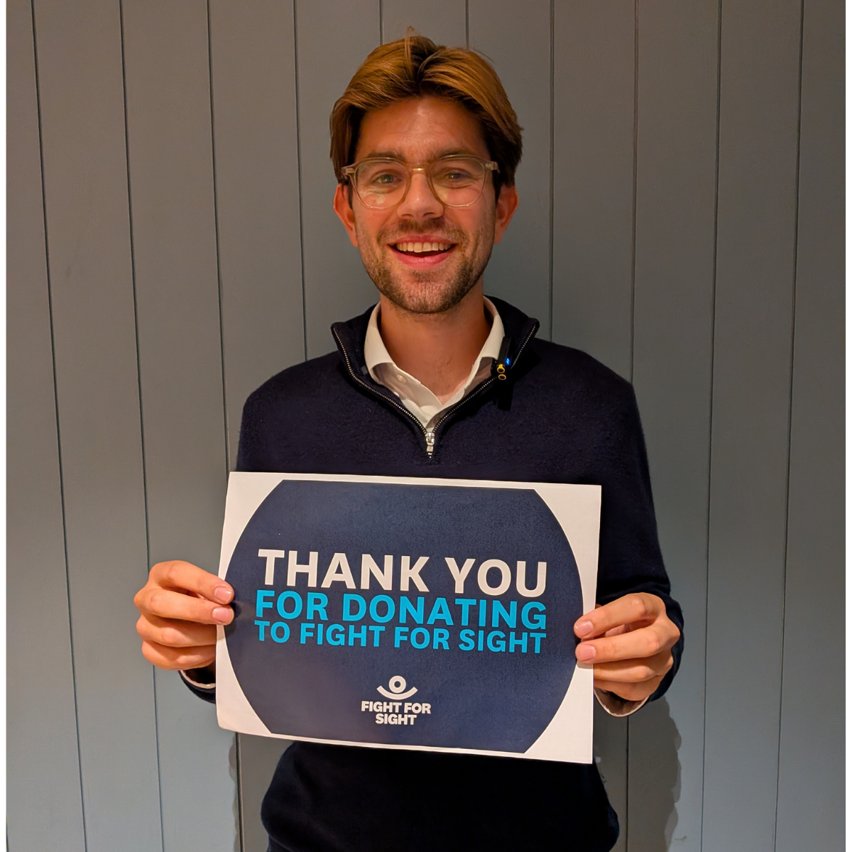 Charlie Shields AK sufferer holding up a sign with e smile on his face, which reads 'Thank for for Donating to Fight for Sight'