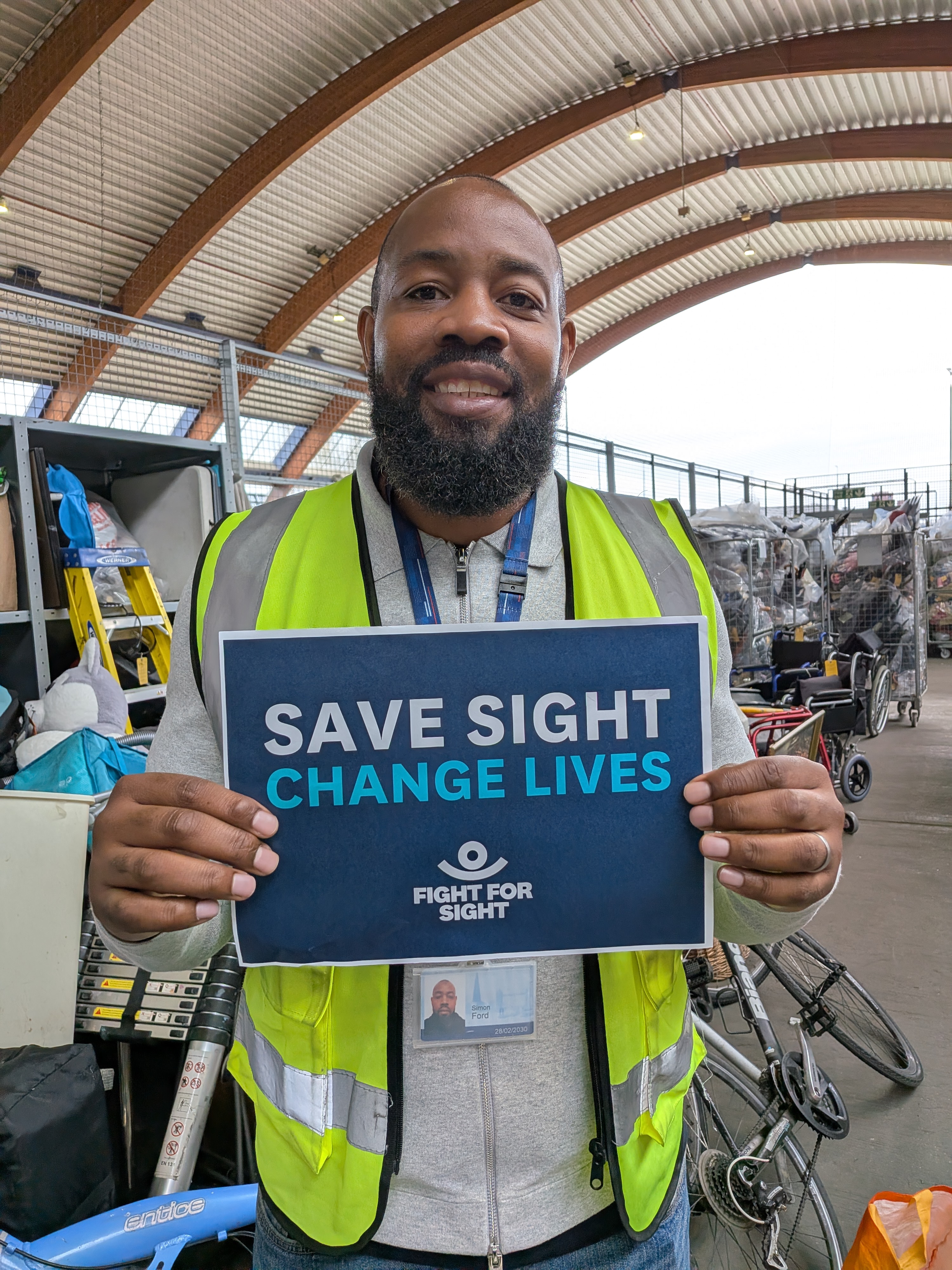 TfL Lost Property donation to Fight for Sight - a friendly looking man in a high vis vest smiles holding up a Fight for Sight poster that says Save Sight. Change Lives.