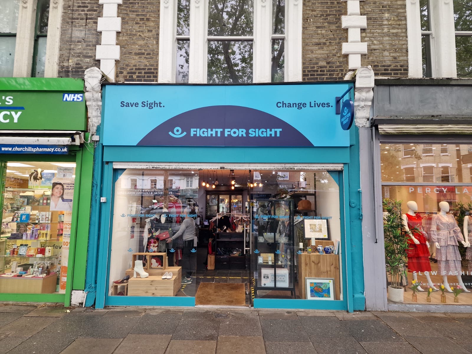 Our Chiswick Charity Shop - Turquoise signage with a navy semi circle that contains the Fight for Sight name and logo and the words Save Sight. Change Lives.