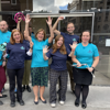A group of Fight for Sight employees standing outside in tshirts in the brand colours - dark navy and teal - they are holding arms aloft and looking cheerful.