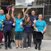 A group of Fight for Sight employees standing outside in tshirts in the brand colours - dark navy and teal - they are holding arms aloft and looking cheerful.