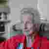 Elizabeth Maxwell in profile - she sits in a chair wearing a red blouse with a blue scarf