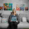 Paula Long, a stylish blonde lady who has been diagnosed with Glaucoma surrounded by her artwork.