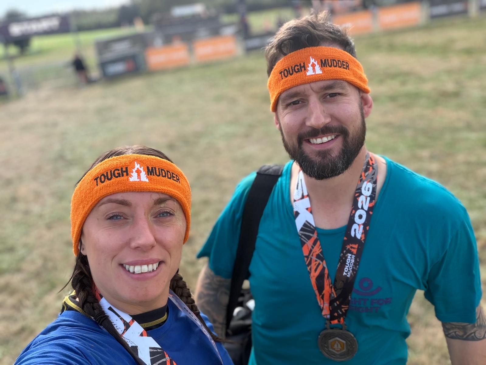 Two participants smiling, proudly wearing their Tough Mudder medals and headband
