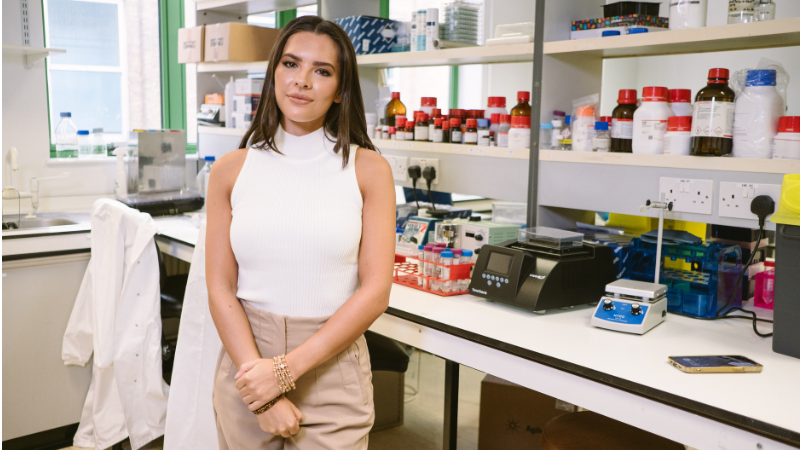 A photo of Gemma Owen in a laboratory. She has long brown hair.