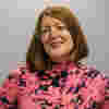 Emma has shoulder lenght red hair and wears a bright top. She is smiling for the camera. 