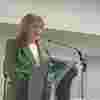 Fiona Sandford CEO of Visionary introducing the conference in 2024. She stands behind a podium and wears a striking green jacket