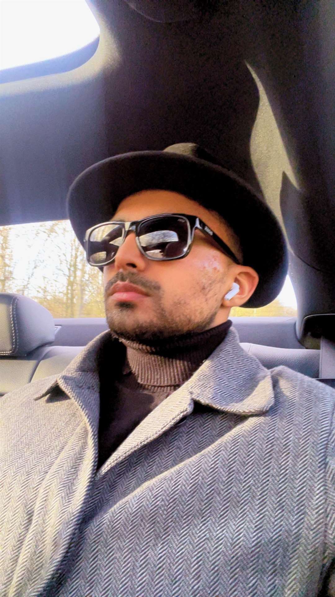 Ibraheem sits in a car - he wears a trilby-style hat and dark glasses. 