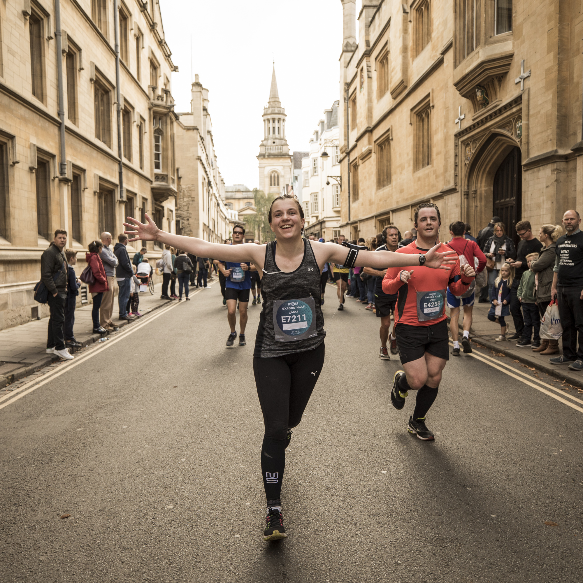 A lady smiling while running through the streets of Oxford with her arms outstretched as she takes part in the Oxford Half Marathon