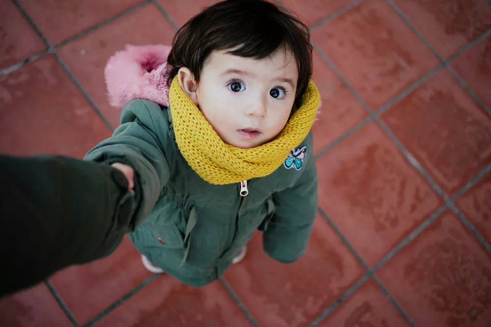A little girl looking up at someone whose hand she's holding.