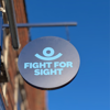 Fight for Sight hanging sign, a navy blue circle with our logo in the centre, with a blue sky behind.