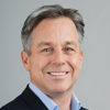 A headshot of Mike Buckley, CEO of BeMyEyes. Mike is smiling and wears a dark blue jacket and a light blue suit.