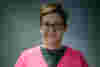 Beck is a white woman with short hair and glasses. She wears a bright pink cardigan. 