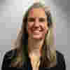 Kim has shoulder-length grey hair and smiles warmly in a medium-shot portrait.  The image presents a straightforward portrait of a woman, centered within the frame.  The woman's expression is one of warmth and friendliness.  The lighting is even and highlights her features without harsh shadows.