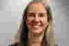 Kim has shoulder-length grey hair and smiles warmly in a medium-shot portrait.  The image presents a straightforward portrait of a woman, centered within the frame.  The woman's expression is one of warmth and friendliness.  The lighting is even and highlights her features without harsh shadows.