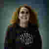 Sarah is a white woman with long ginger hair and wear a baggy stripey jumper. 