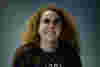 Sarah is a white woman with long ginger hair and wear a baggy stripey jumper. 