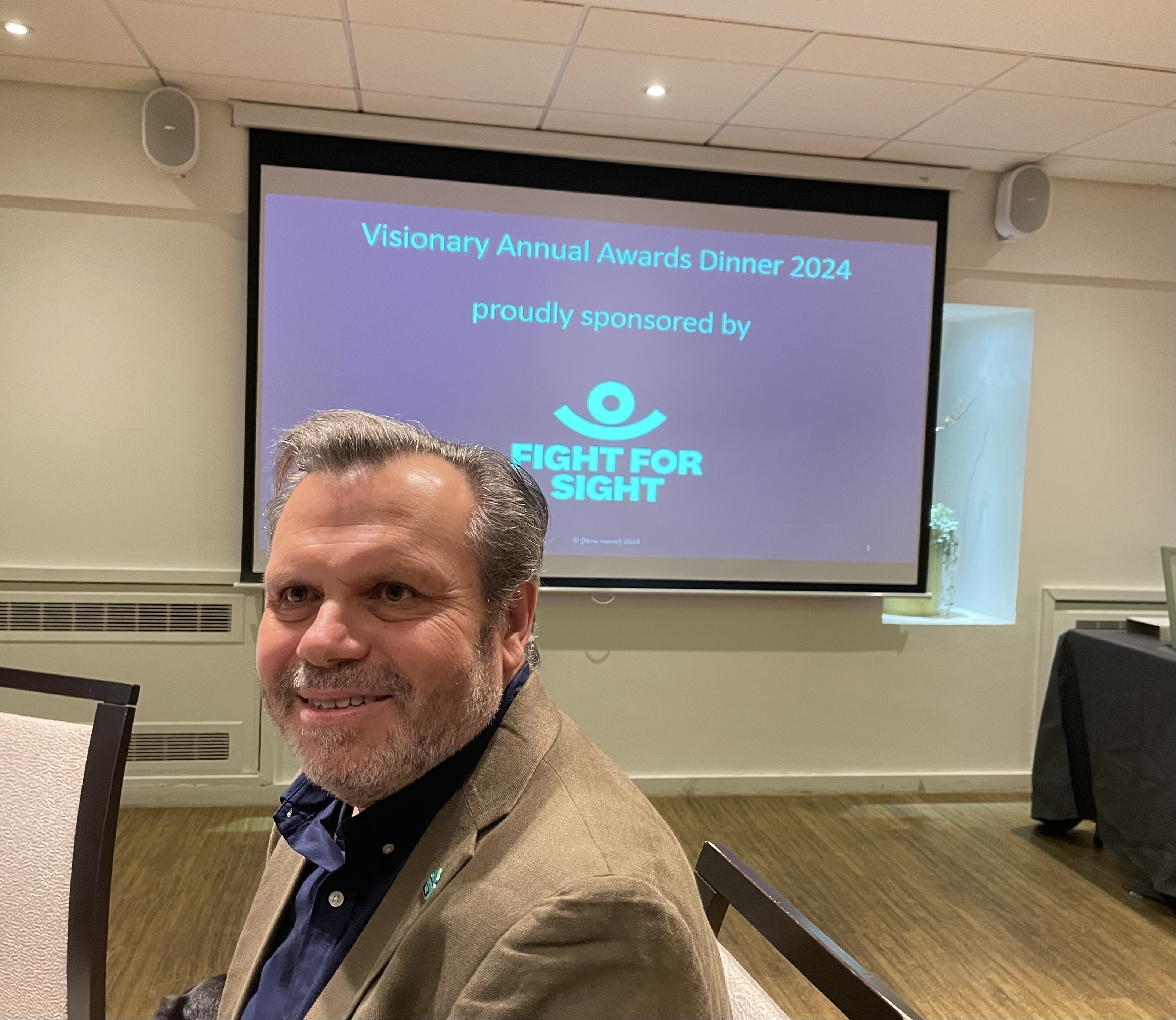 Fight for Sight CEO, Keith Valentine, sitting in front of a display that reads: Visionary Awards dinner 2024, proudly sponsored by Fight for Sight