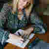 Paula Long, a stylish blonde lady who has been diagnosed with Glaucoma writing at a desk.