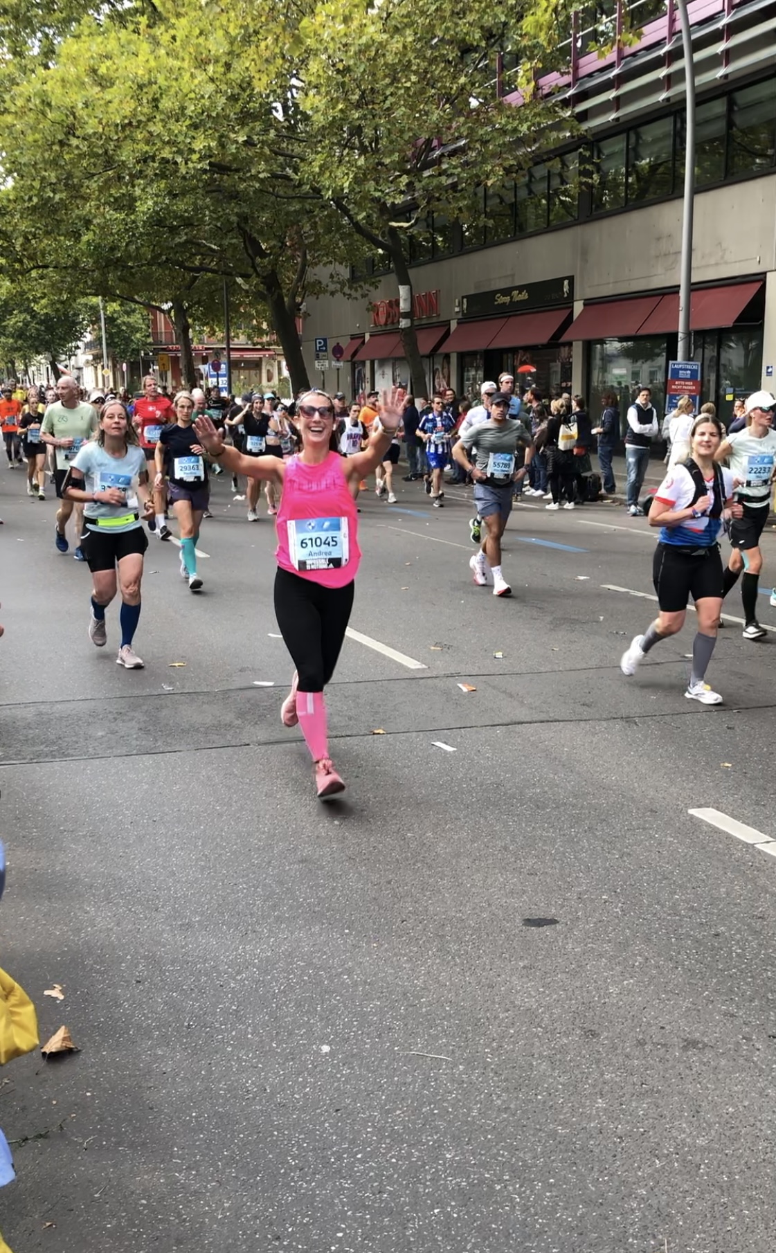 Andrea in a bright pink running vest is running in an event, her arms are raised and she's smiling