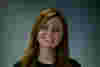 A picture of Fran wearing a black jumper. She is a young white woman with red hair. Her hands are clasped in front of her. 